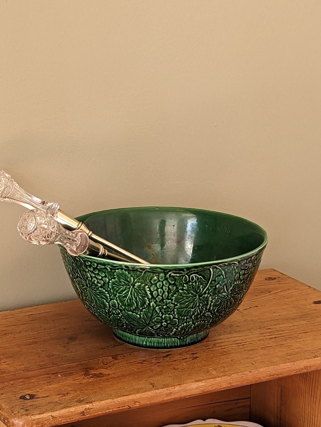 green majolica bowl with serving tongs on wooden shelf